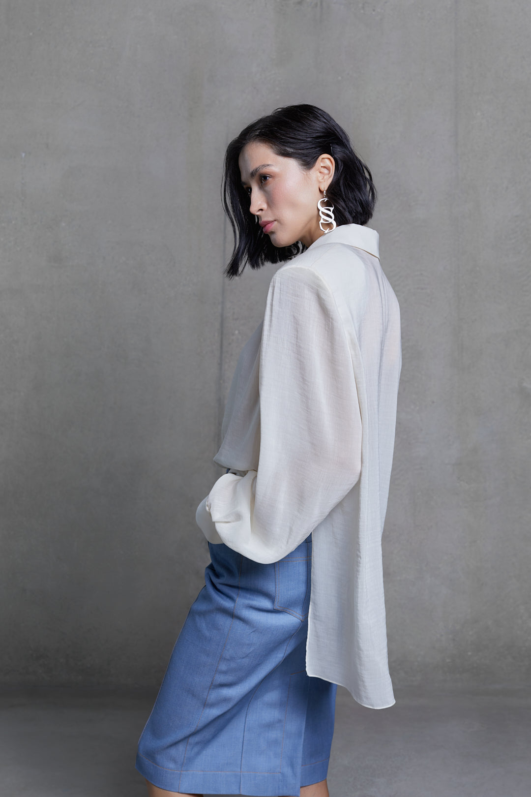 Side view of white designer wool blouse showing draped sleeve and minimal tailoring