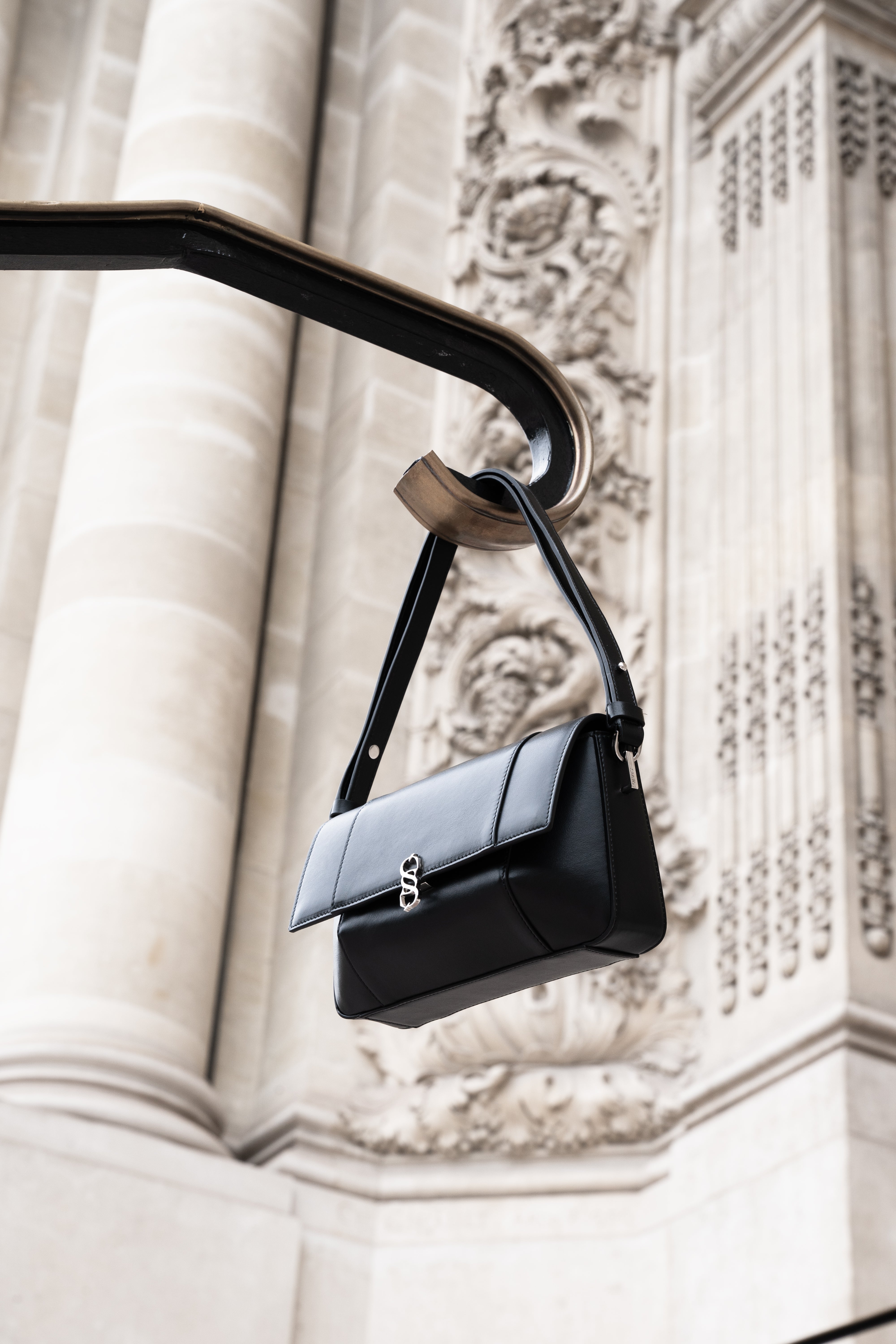 Black Il Cupola leather bag suspended from a curved railing against carved stone architecture