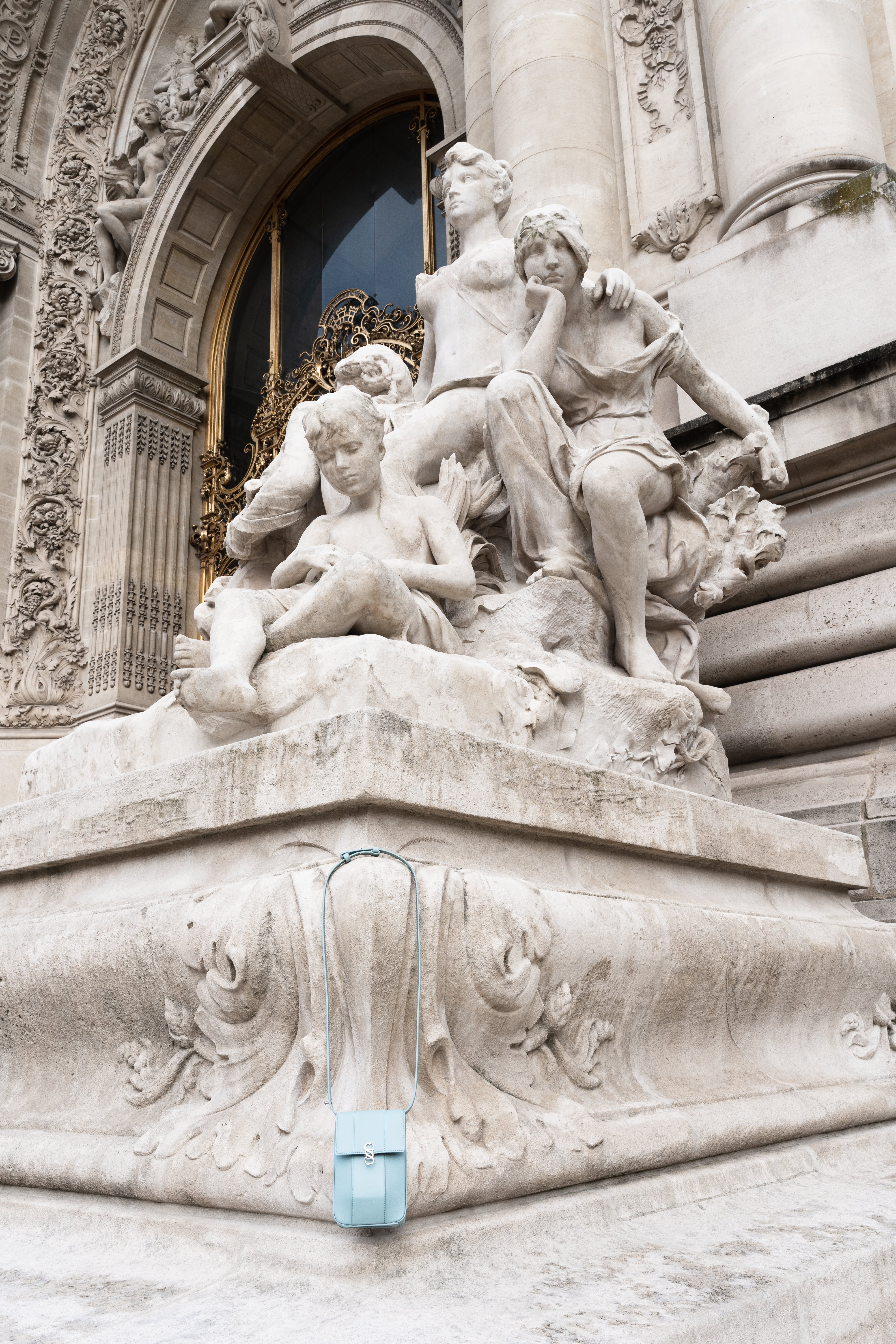 Clear aqua Il Cupolina leather bag styled against carved stone architecture, long strap and flap