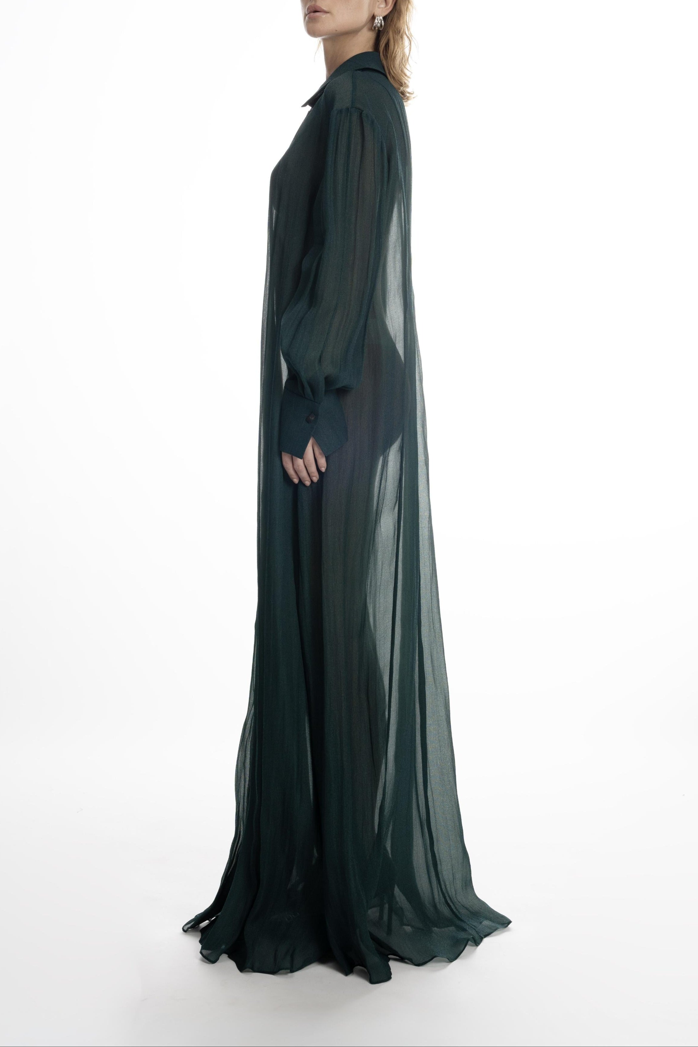 Deep green silk long shirt dress with long cuffs and fluid, semi-sheer drape. Side view