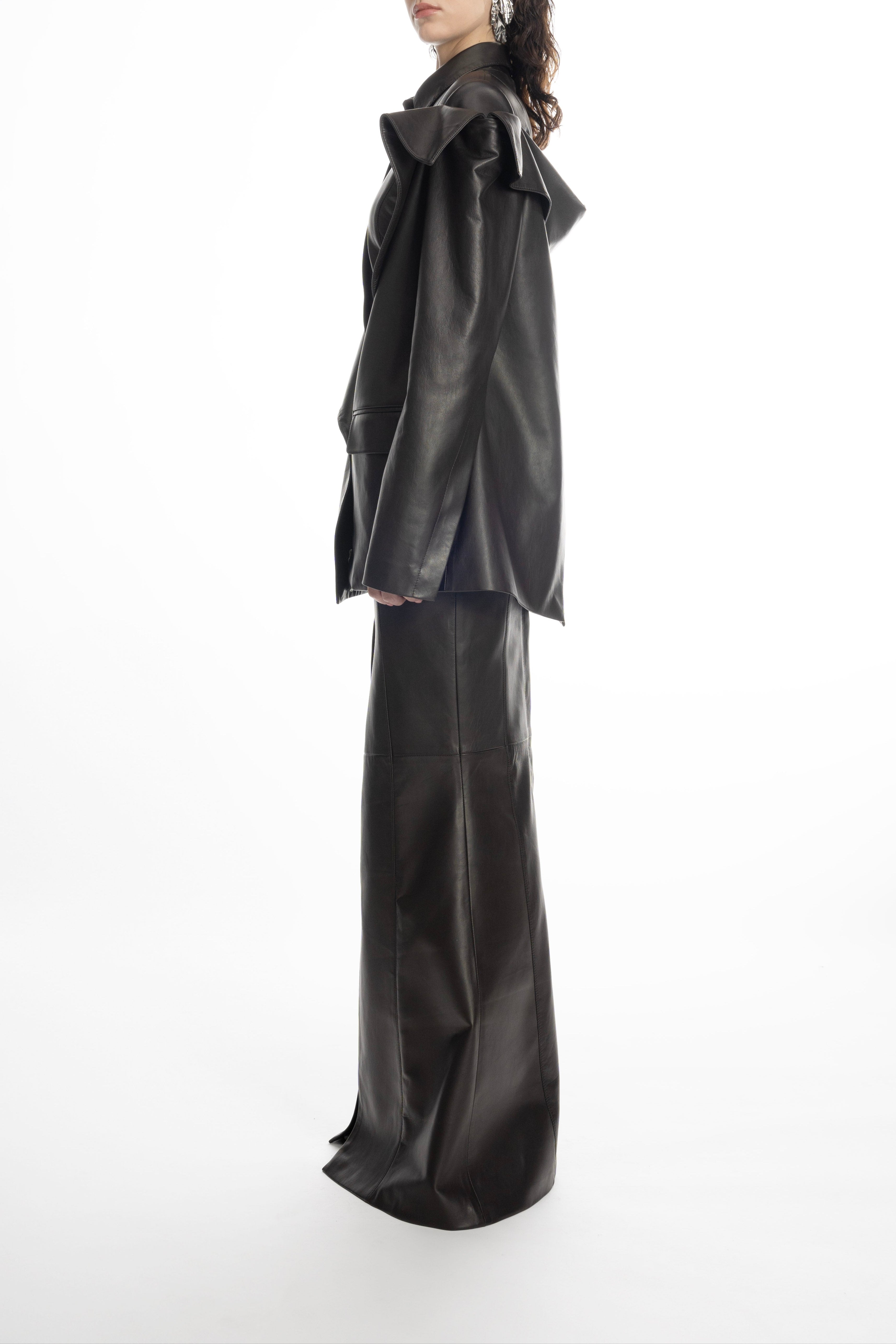 Woman wearing the sculptural black leather jacket styled with a matching long leather skirt.