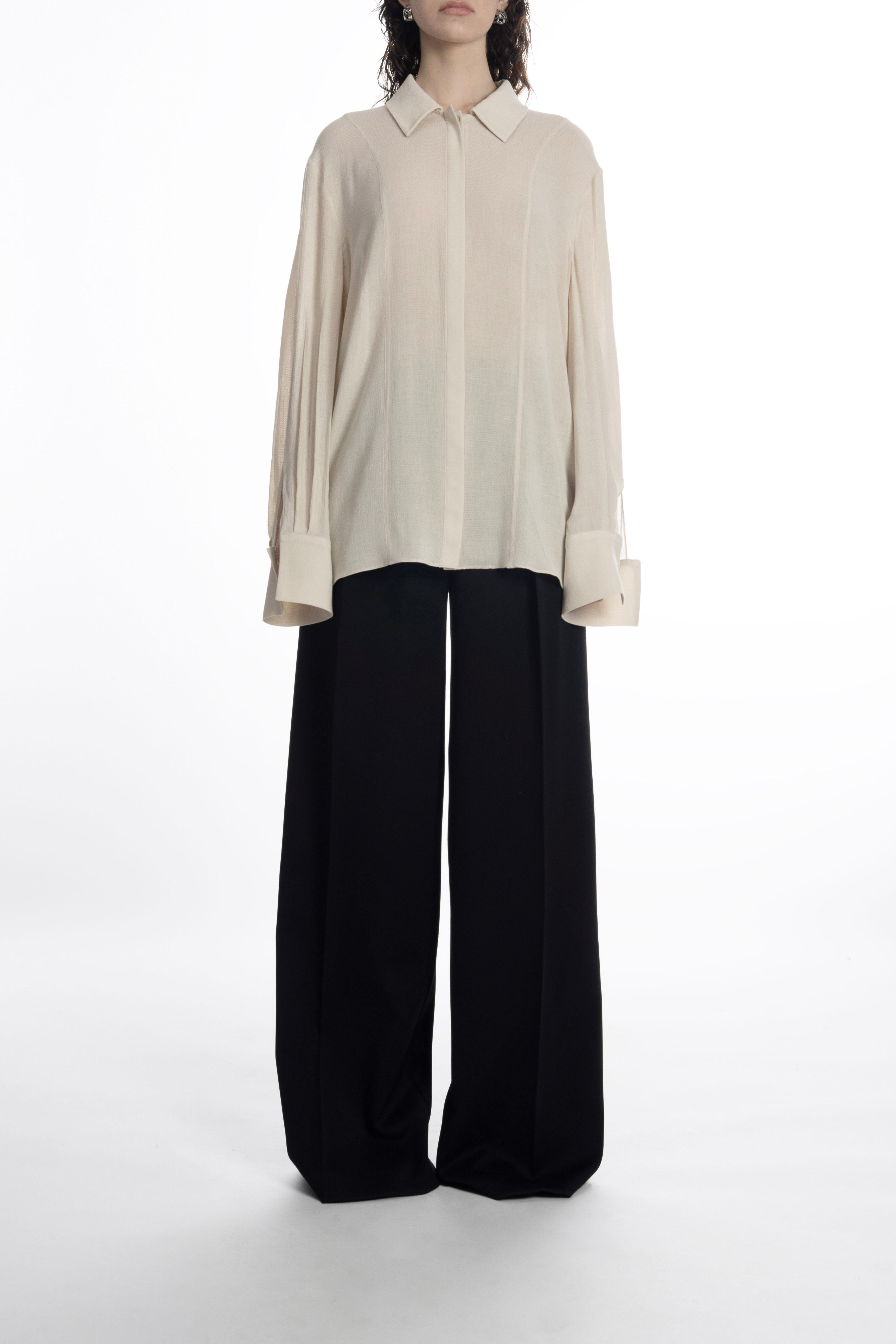 Model wearing ivory long-sleeve classic blouse with concealed placket and wide-leg black trousers.