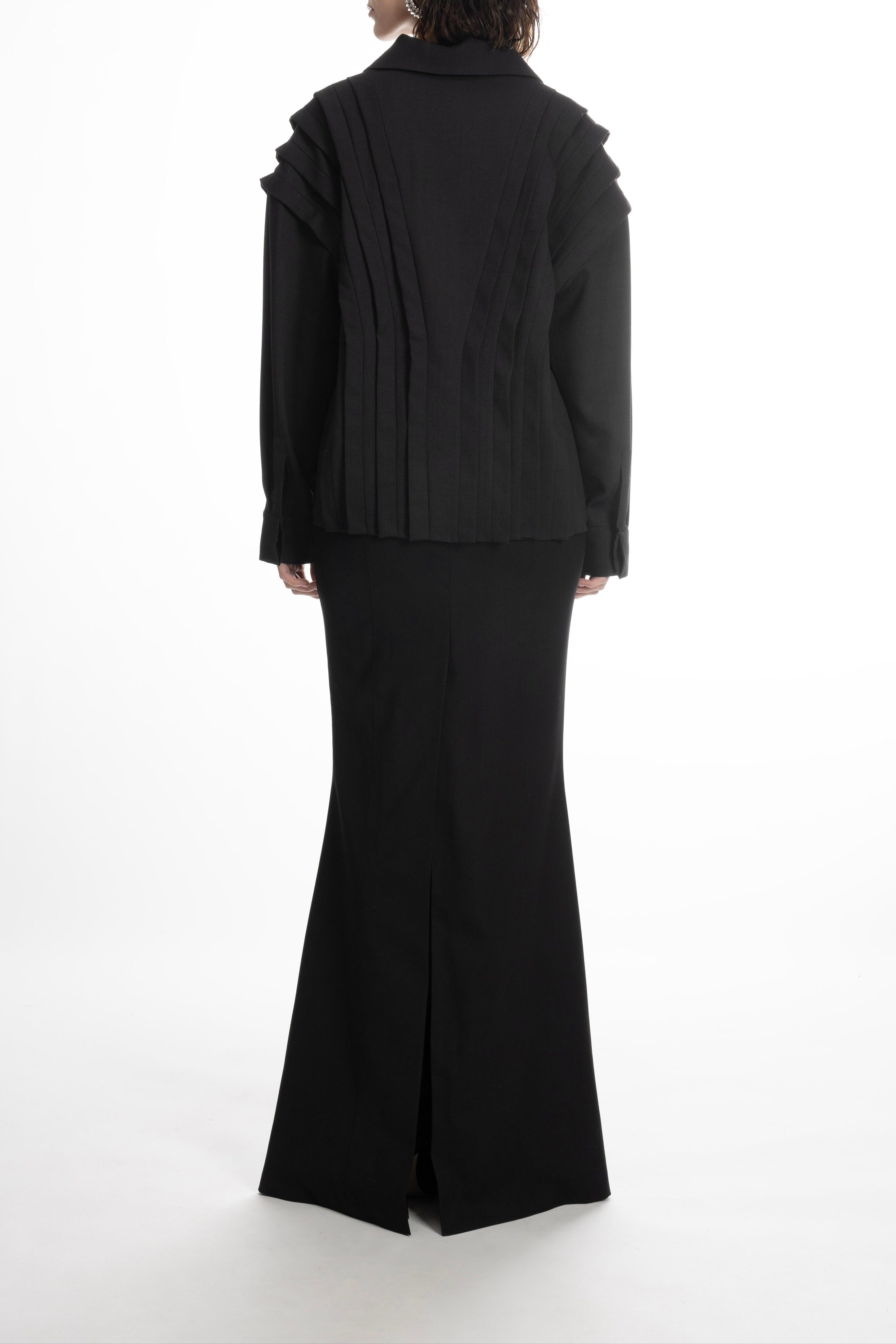 Blouse with layered pleated panels, collar and long sleeves, styled with floor-length skirt.