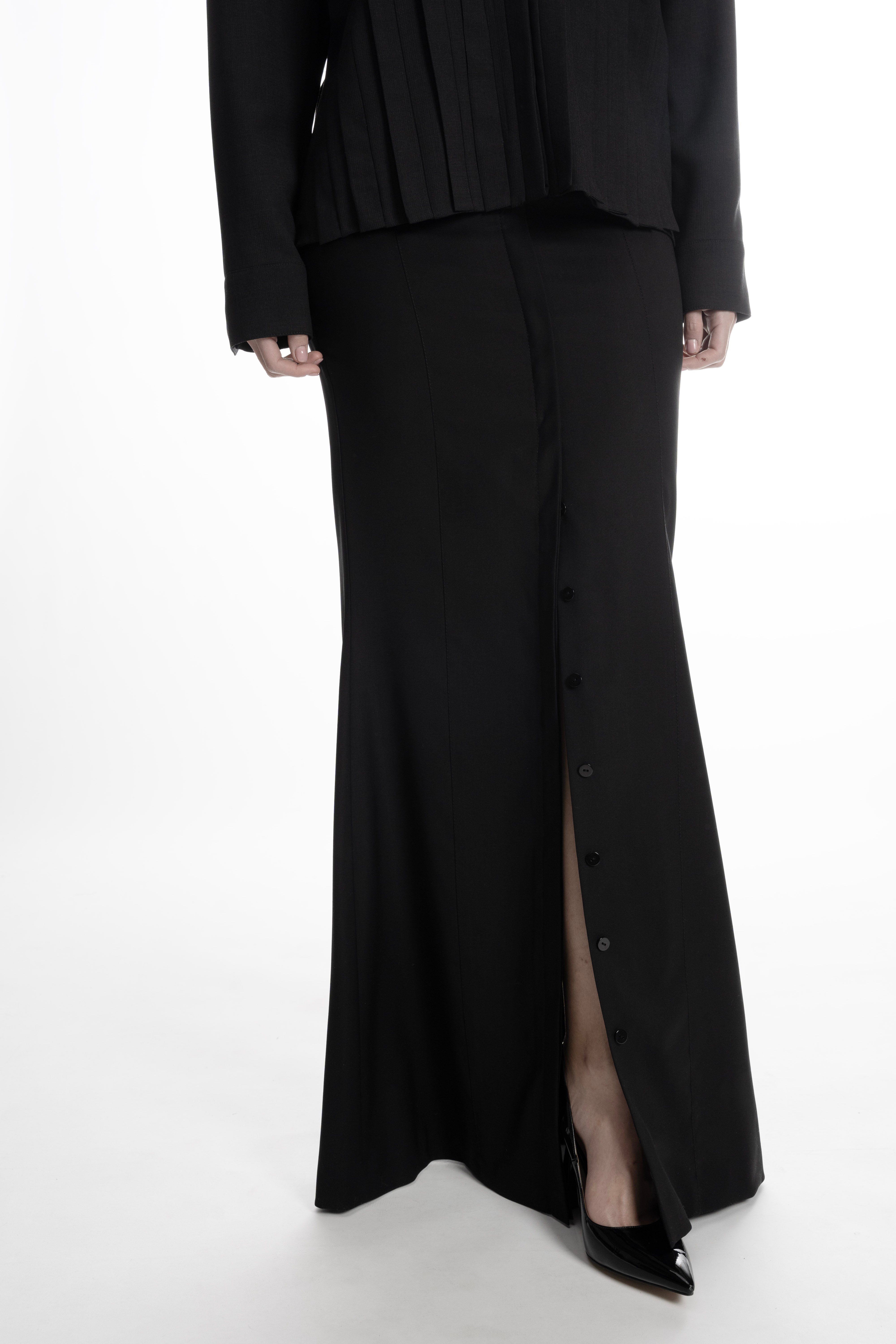 Close-up of buttoned placket opening at the hem of the black skirt.