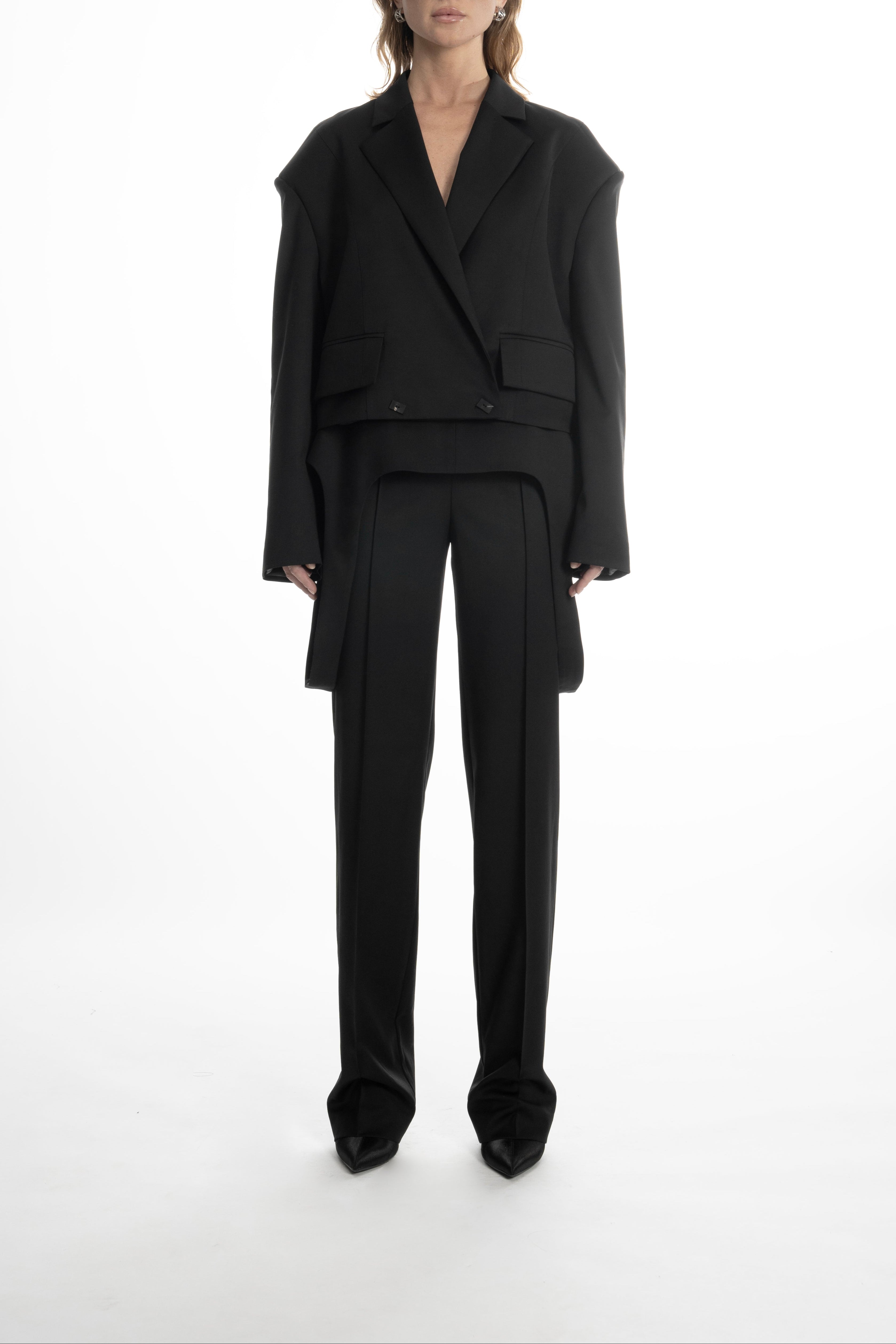 Woman wearing a black cropped wool blazer and tailored trousers, highlighting sculptural shoulders.