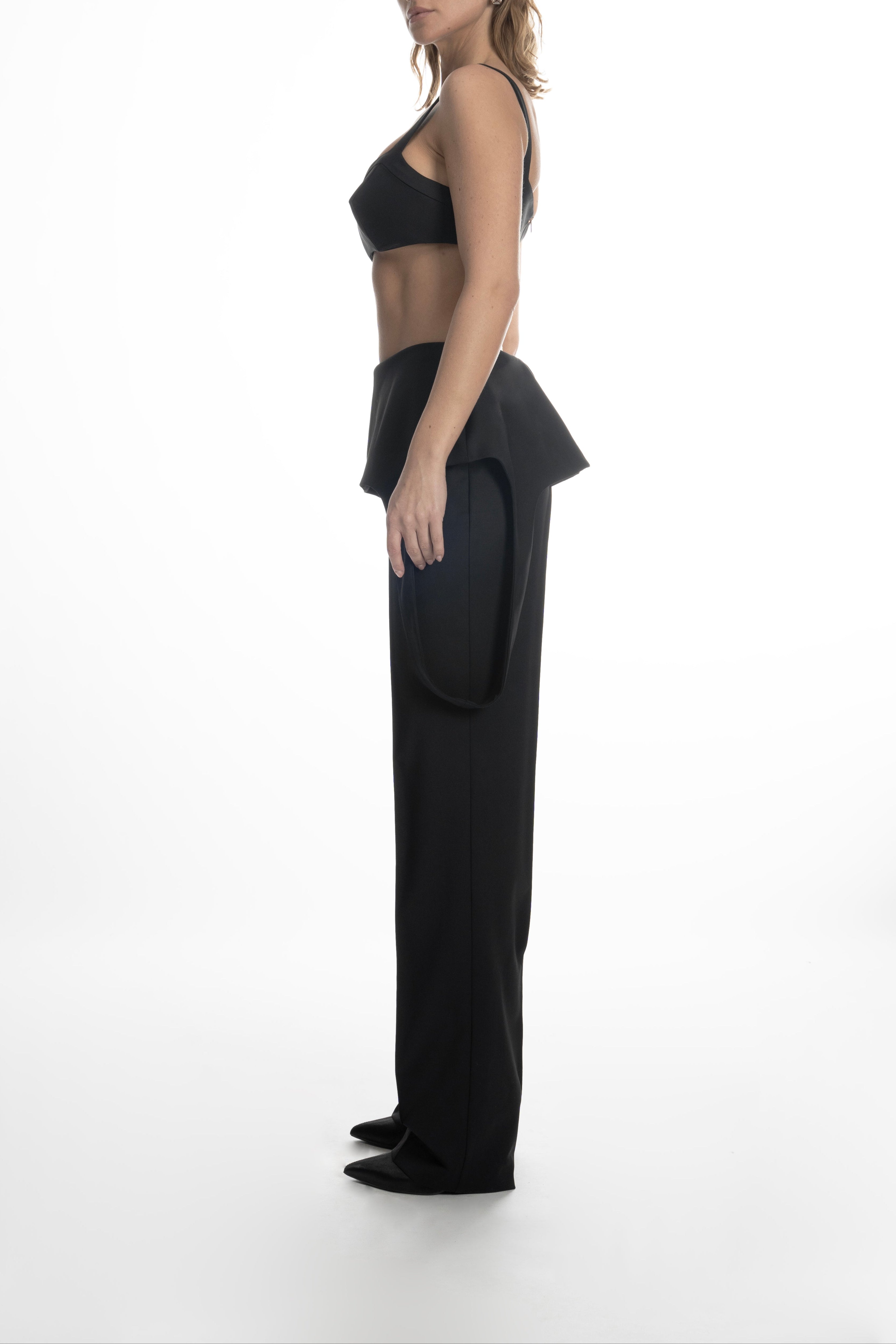 Side view of model in black high-waist wool trousers highlighting the profile of sculptural hip panels and elongated straight leg