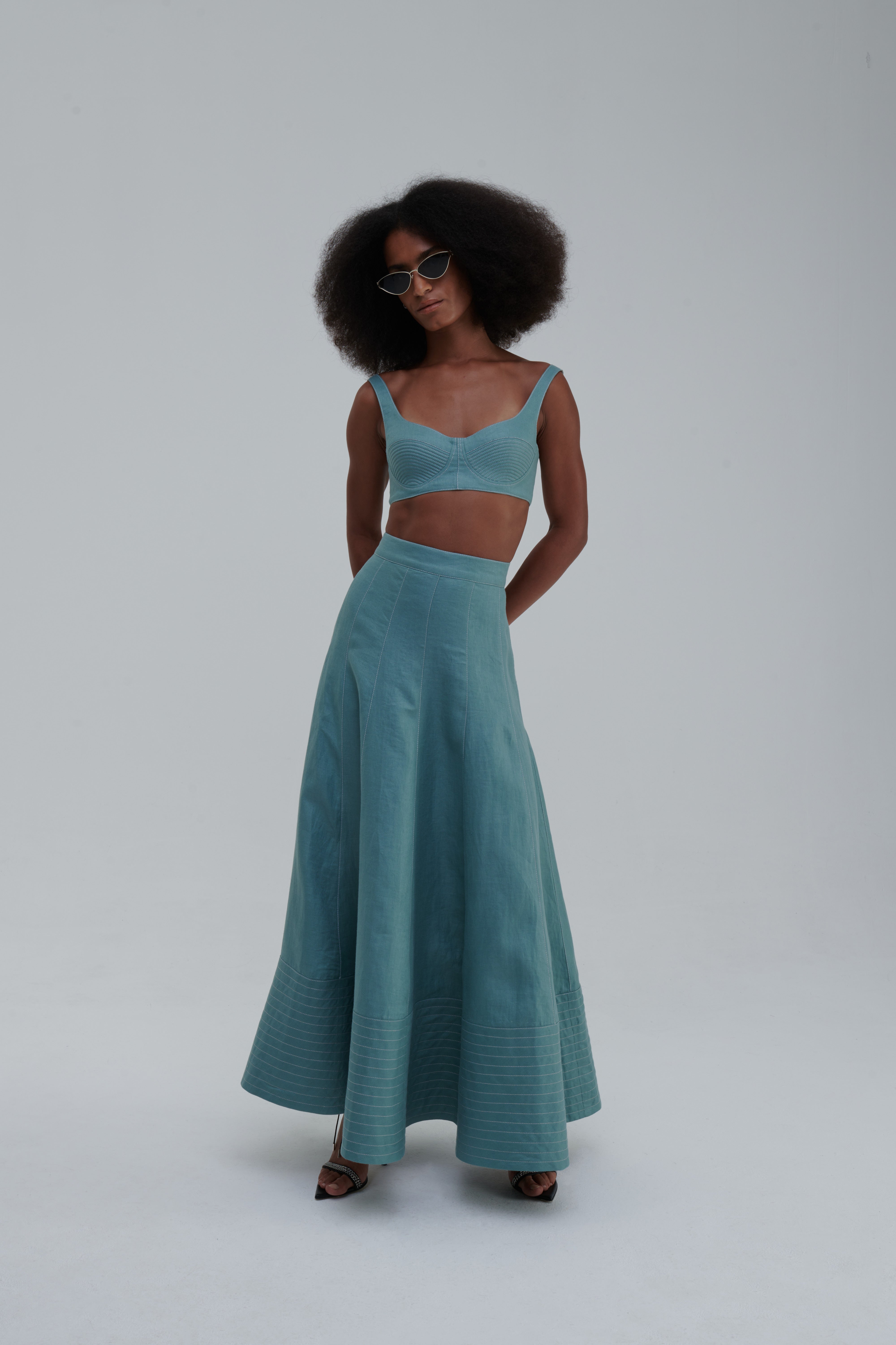 QUILTED LINO SKIRT by Sagio from the Spring/Summer 2025 collection — a mid-length beige linen skirt with subtle quilted paneling, clean lines, and a structured minimalist silhouette. Refined and contemporary womenswear from thesagio.com