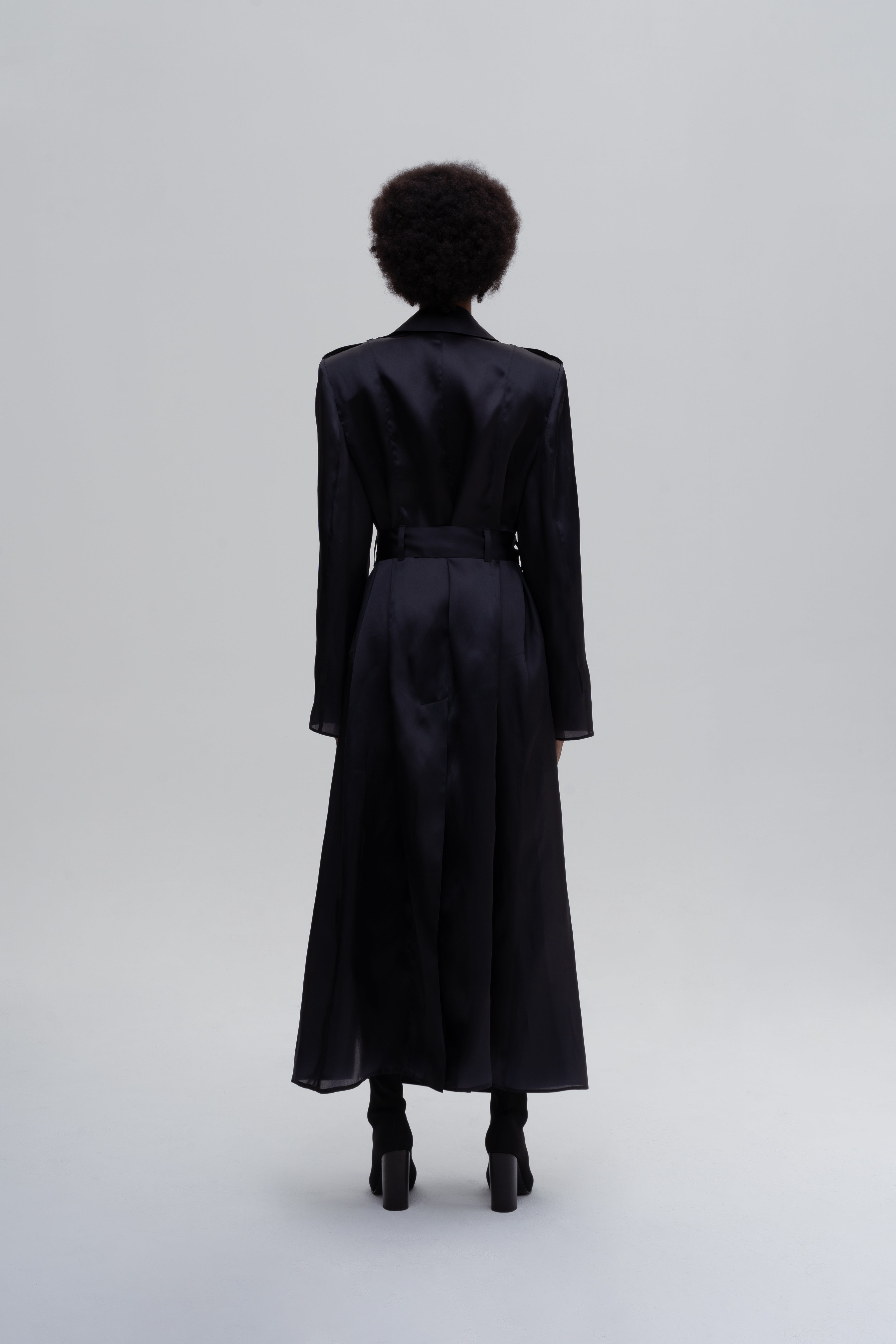 Women’s black silk trench coat with belt and longline silhouette, back view on model