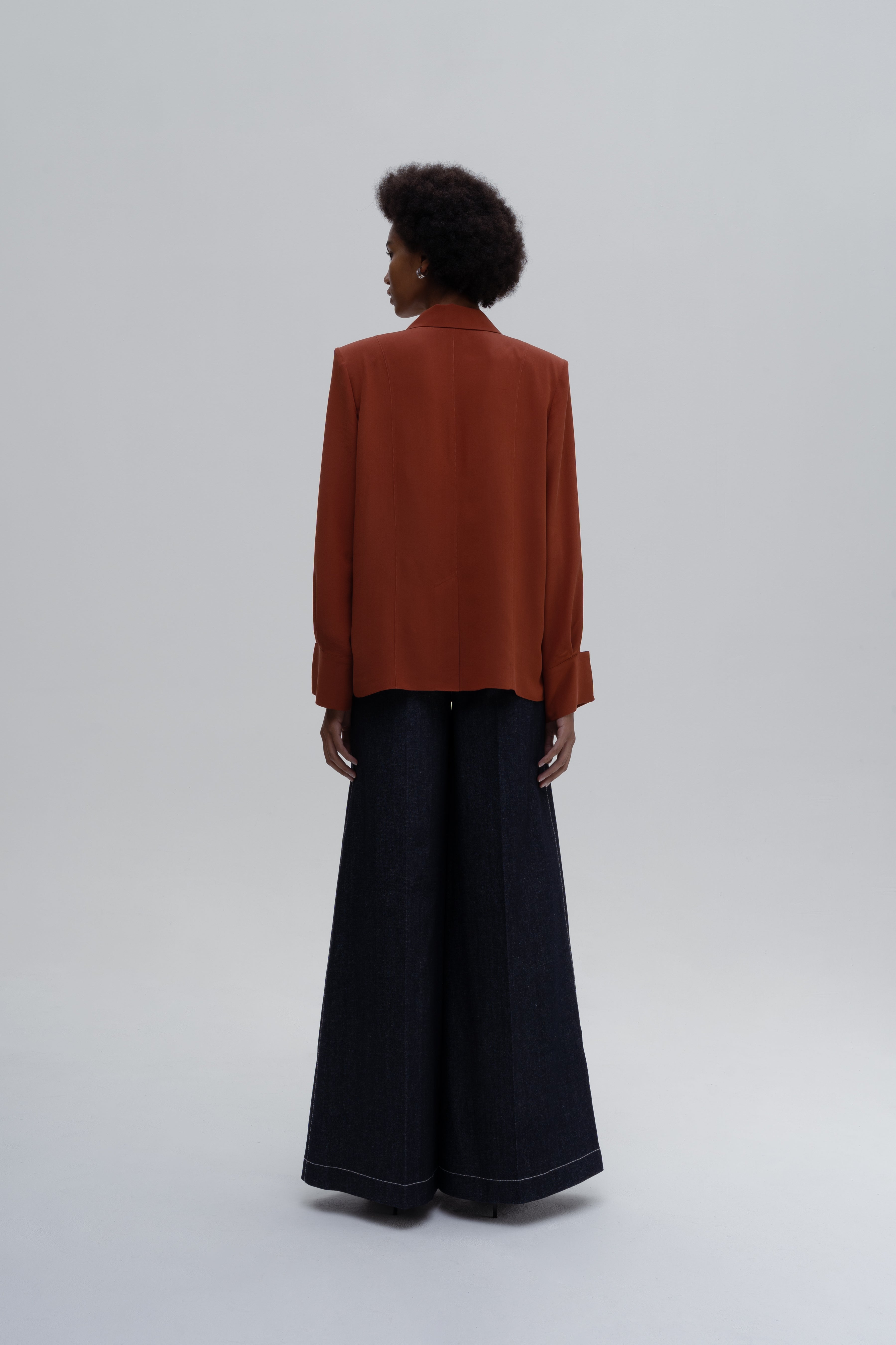 Model wearing the Silk Shirt by Sagio from the Spring/Summer 2025 collection, featuring a relaxed-fit, long-sleeve red silk blouse with a classic collar and concealed button placket. Luxury women's fashion by Sagio — discover more at thesagio.com.