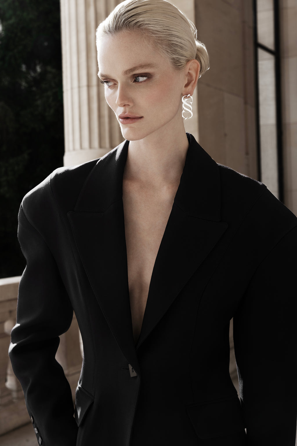 Woman in the black Falling Shoulders Jacket, deep V lapels and relaxed shoulder line, tailored wool silhouette against stone columns