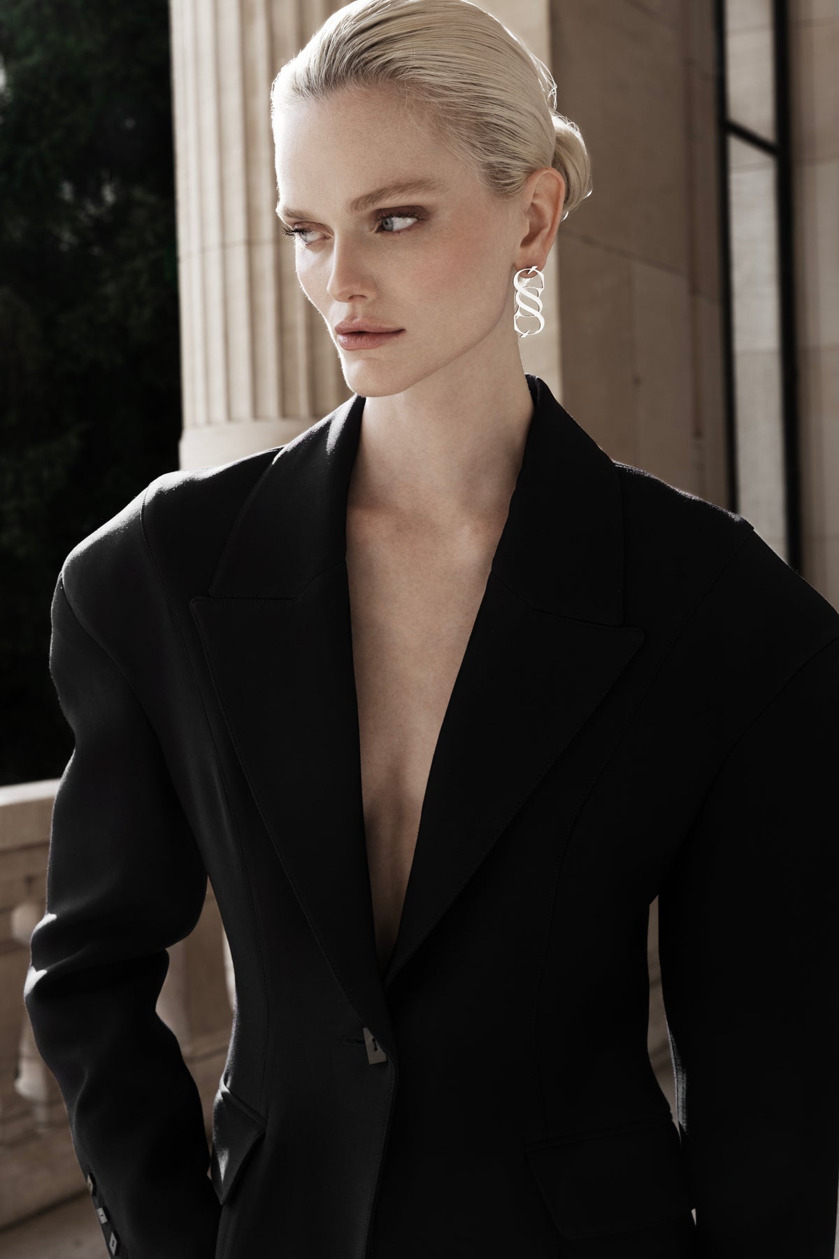 Woman in the black Falling Shoulders Jacket, deep V lapels and relaxed shoulder line, tailored wool silhouette against stone columns