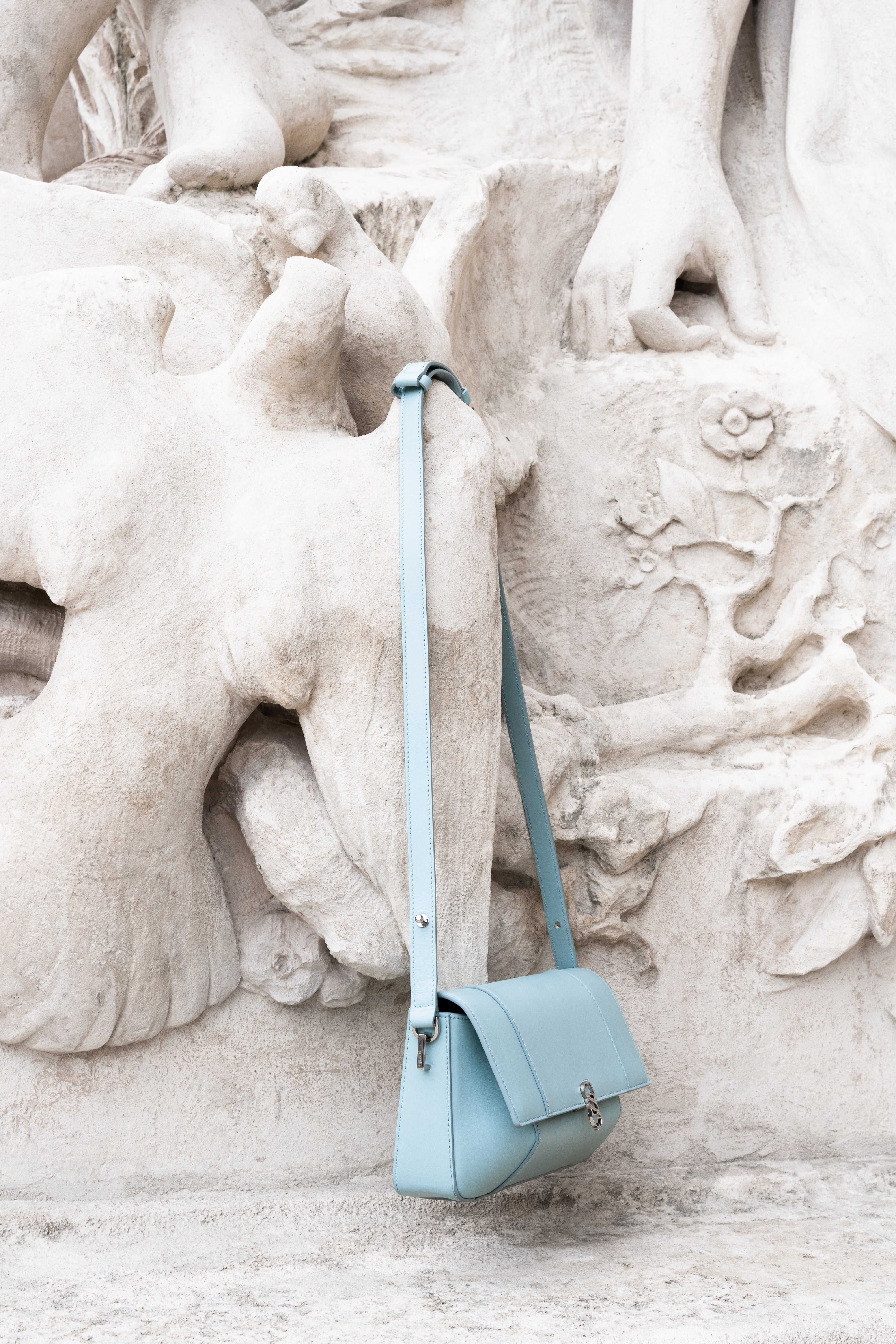 Clear aqua Il Cupola leather bag styled against stone sculpture in side view