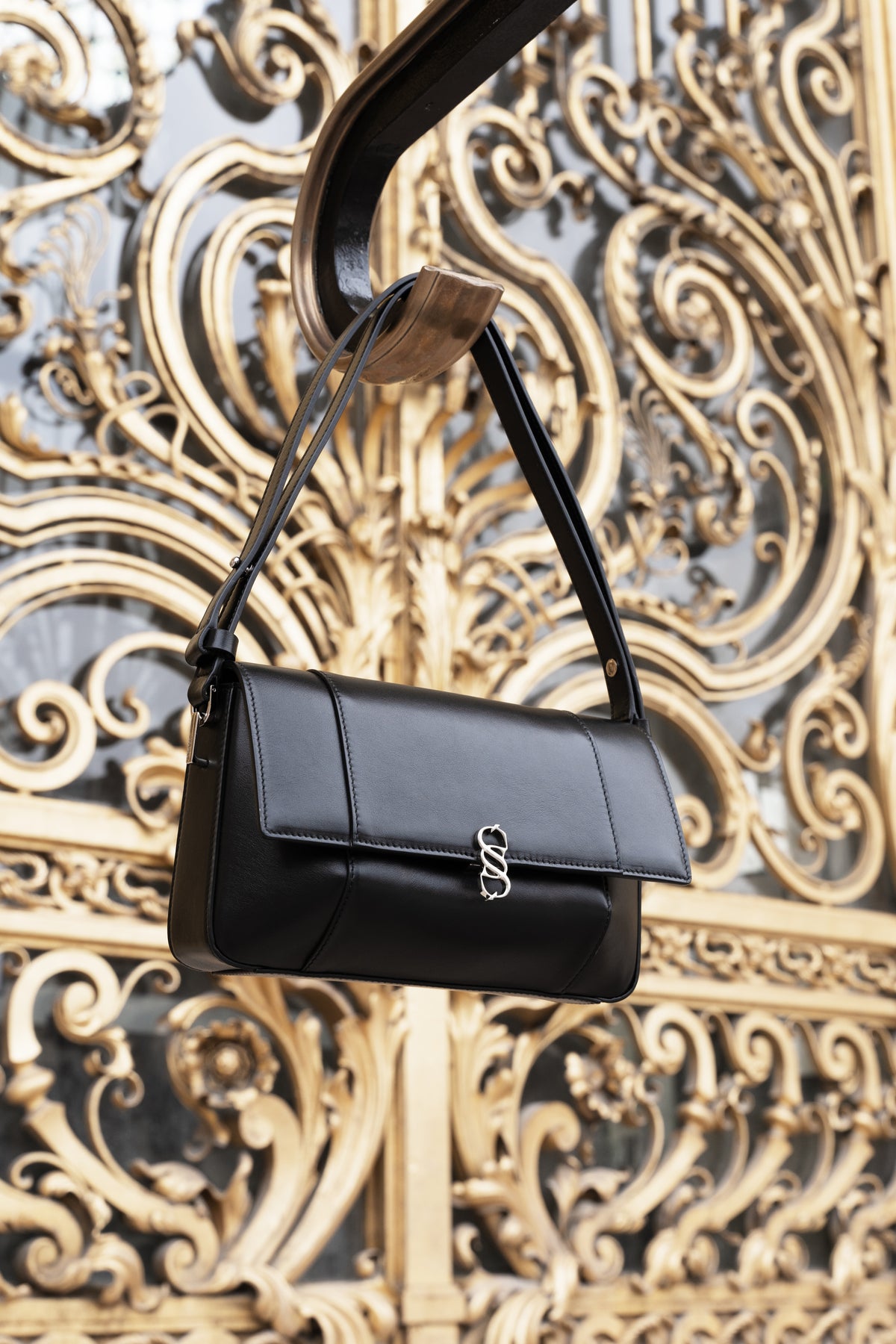Black Il Cupola leather bag suspended against an ornate gold architectural backdrop
