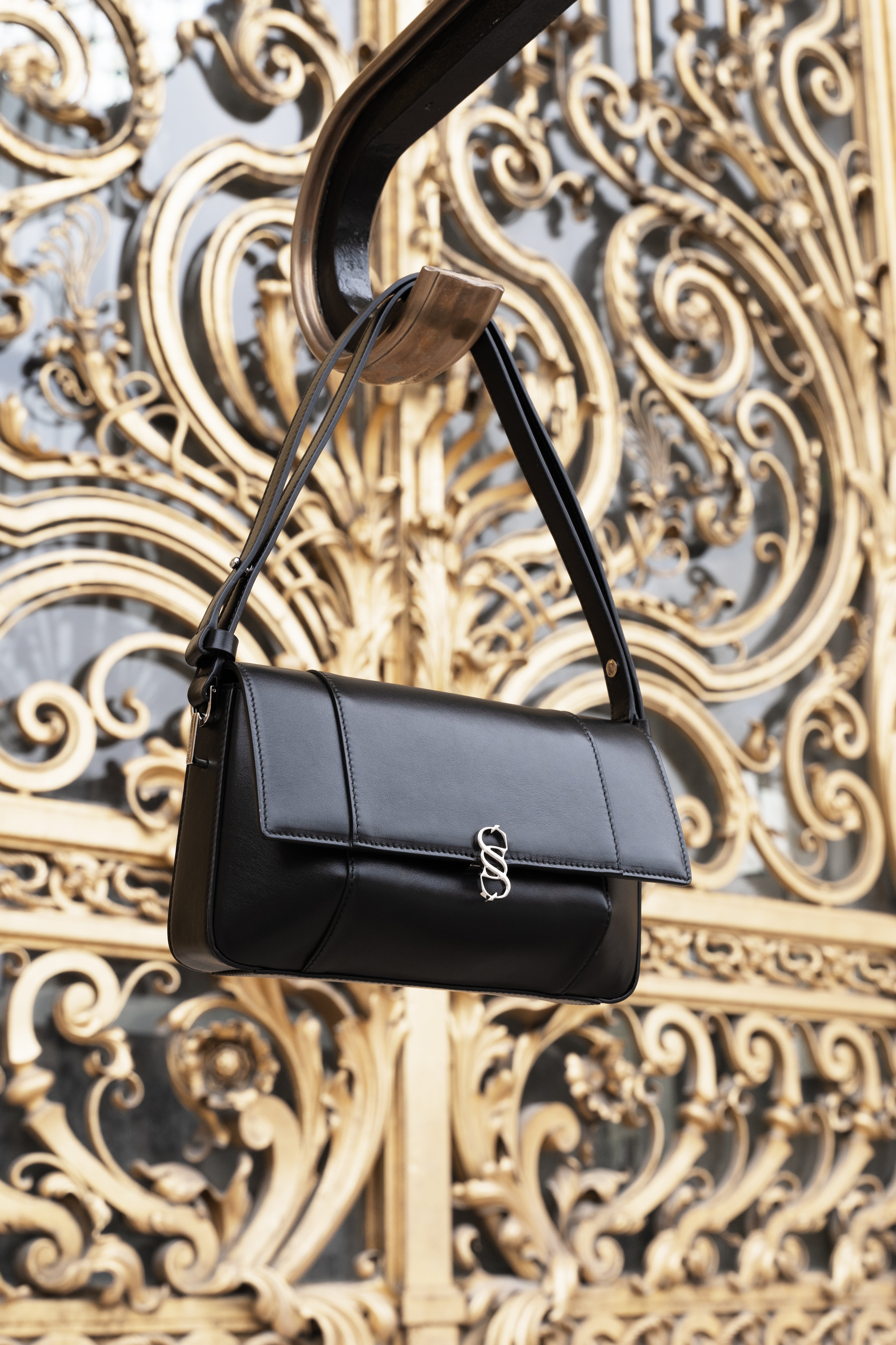 Black Il Cupola leather bag suspended against an ornate gold architectural backdrop