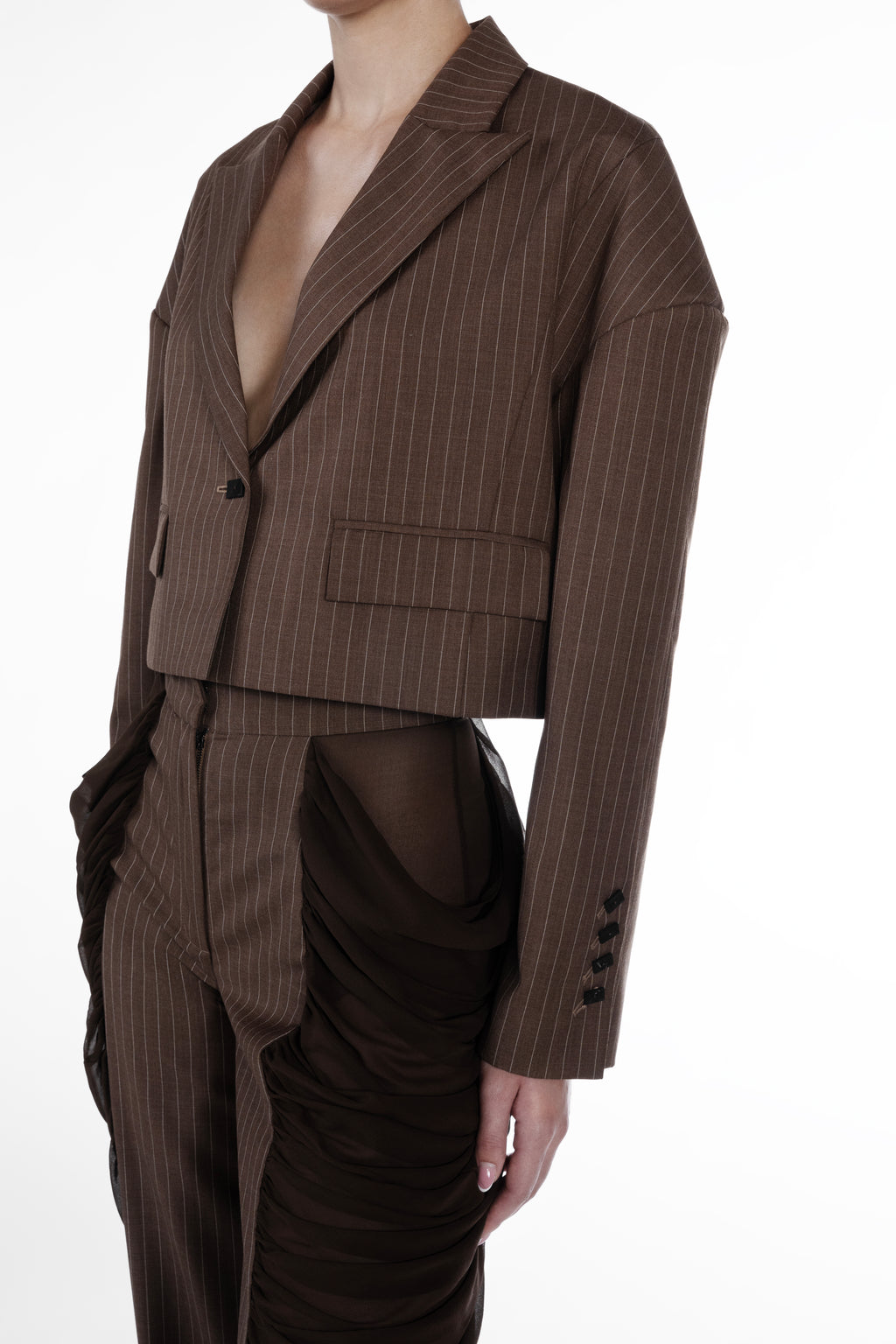 Silk Folds Stripes Trousers in Brown, close-up detail view, pinstriped wool-silk tailoring with sculptural side draping, sheer silk inserts and refined construction. Falling Shoulders Stripes Jacket by SAGIO in brown beige pinstripe wool, detail view, lapel, flap pocket and tailored cropped construction