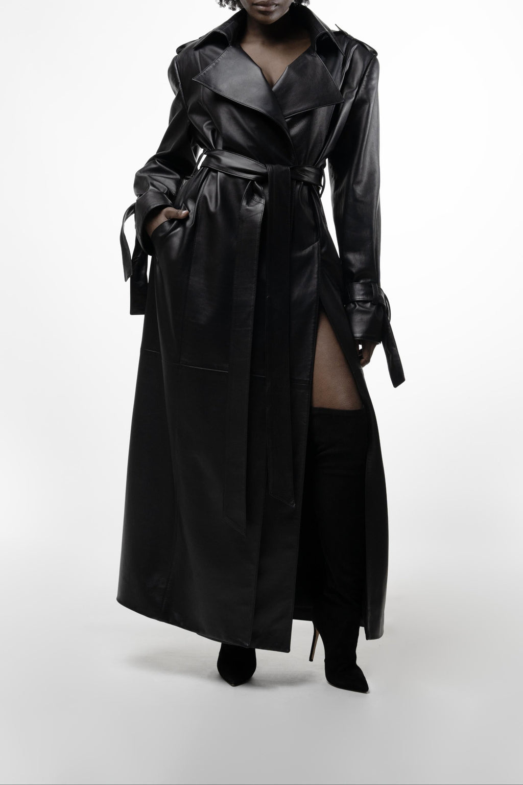 Model wearing long black leather trench with dramatic thigh-high slits