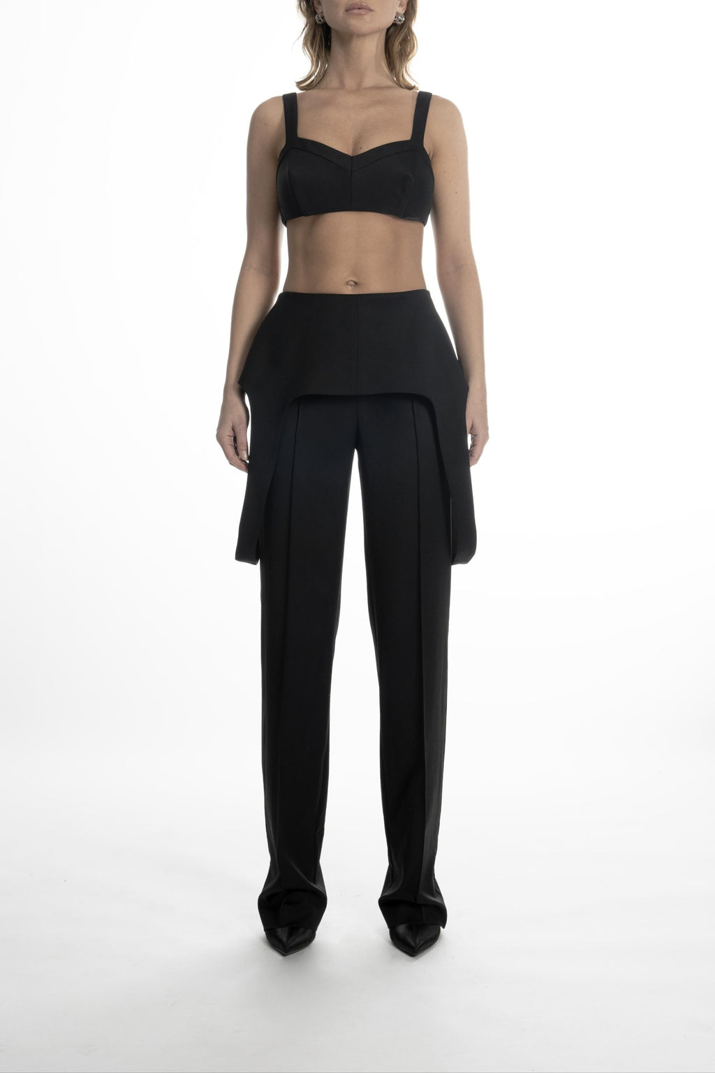 Woman wearing black high-waist wool trousers with sculptural hip panels and long straight legs