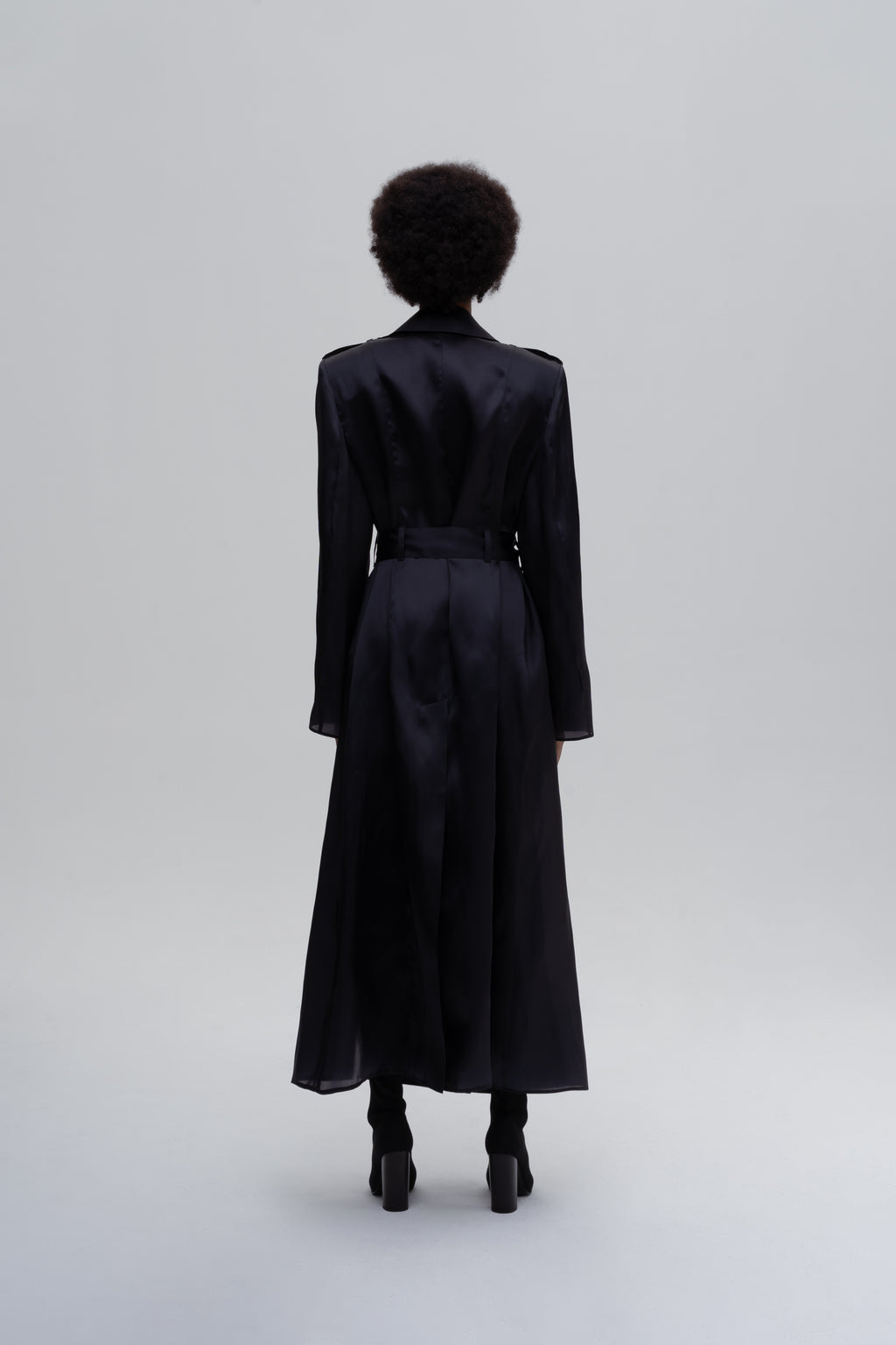 Women’s black silk trench coat with belt and longline silhouette, back view on model