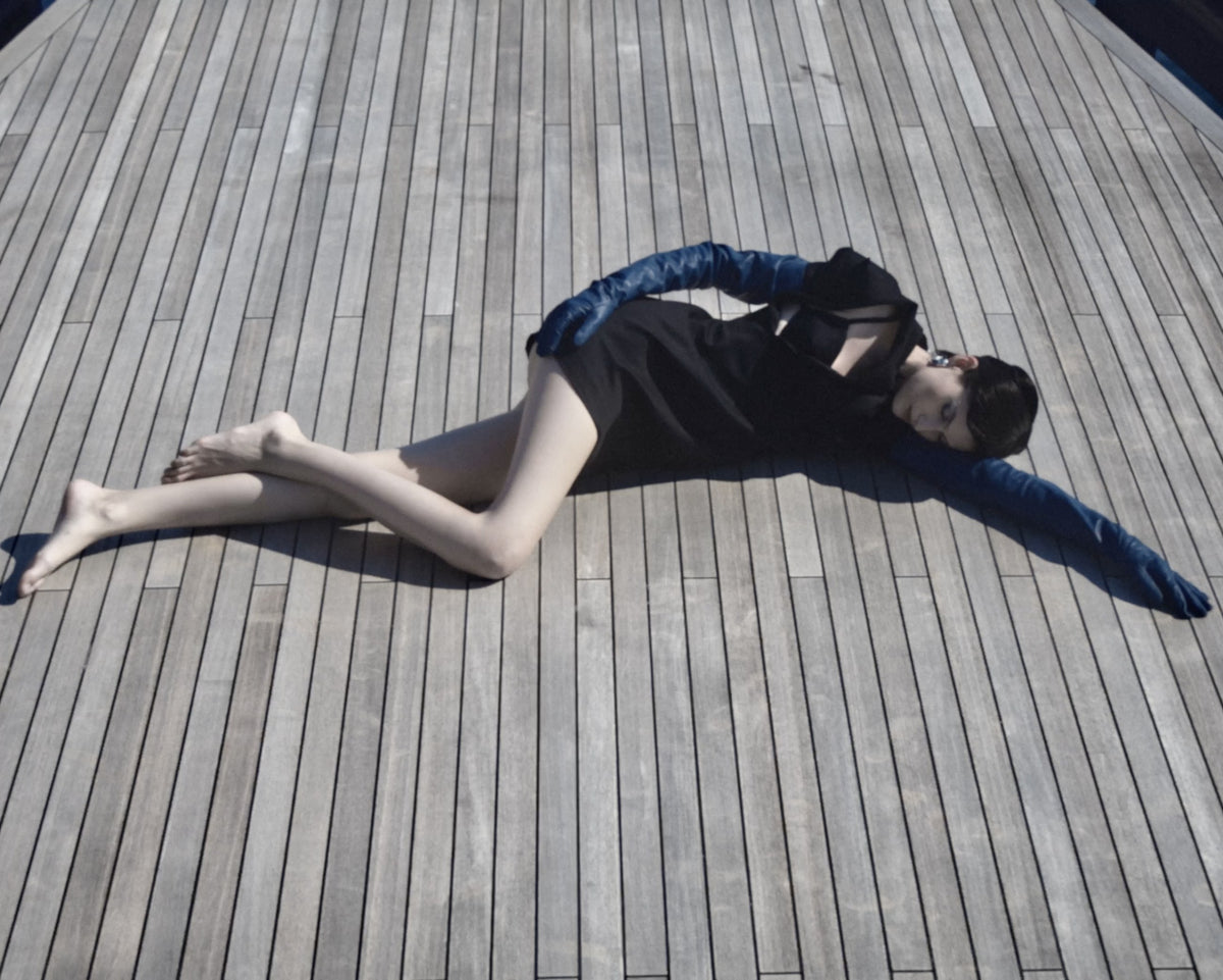 Model lying on a yacht deck in a black dress and blue opera gloves